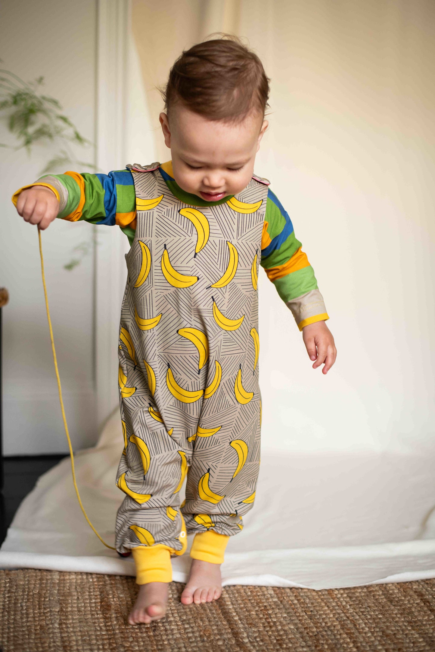 child wearing the baby romper with bananas on a beige background colour fabric of organic cotton jersey